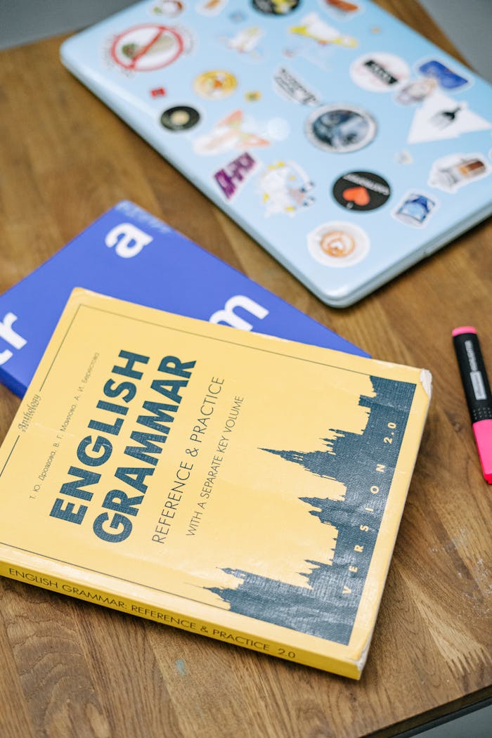 Mastering the First Impression: Your intriguing post title goes here High-angle view of an English grammar book and a laptop with stickers on a wooden desk.